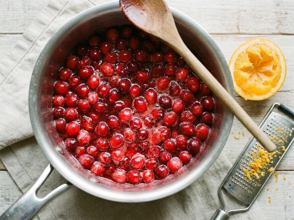 Fresh cranberries simmering in orange juice and sugar in a saucepan, some berries burst