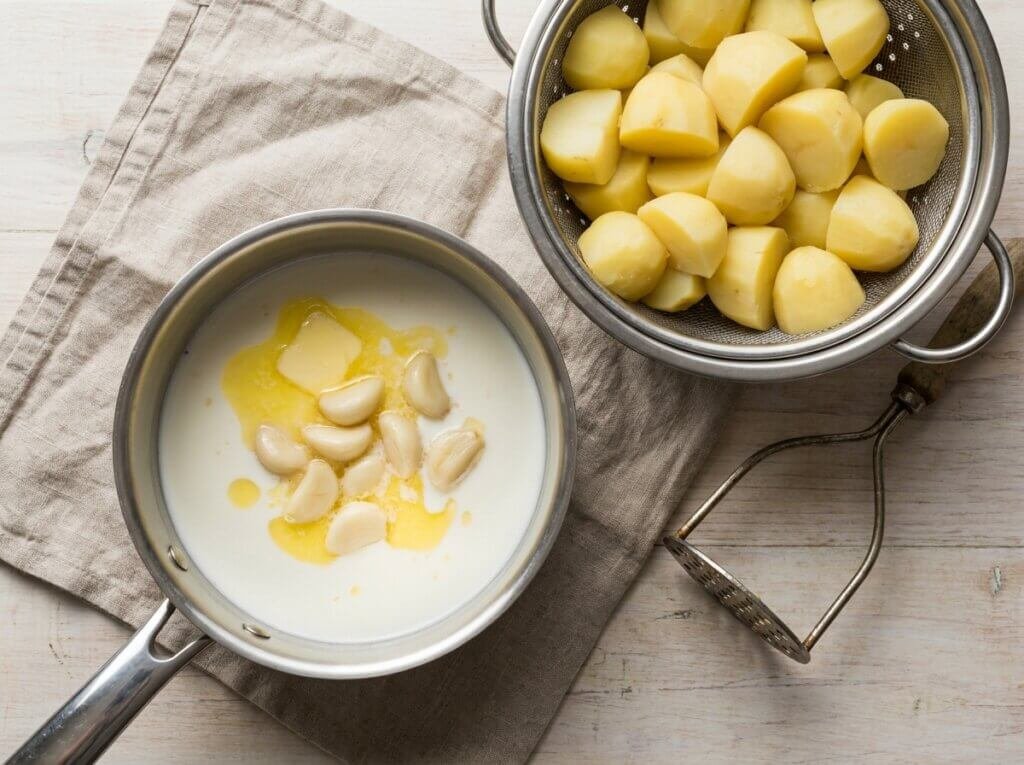 Whole garlic cloves softening in warm milk and butter in a small saucepan