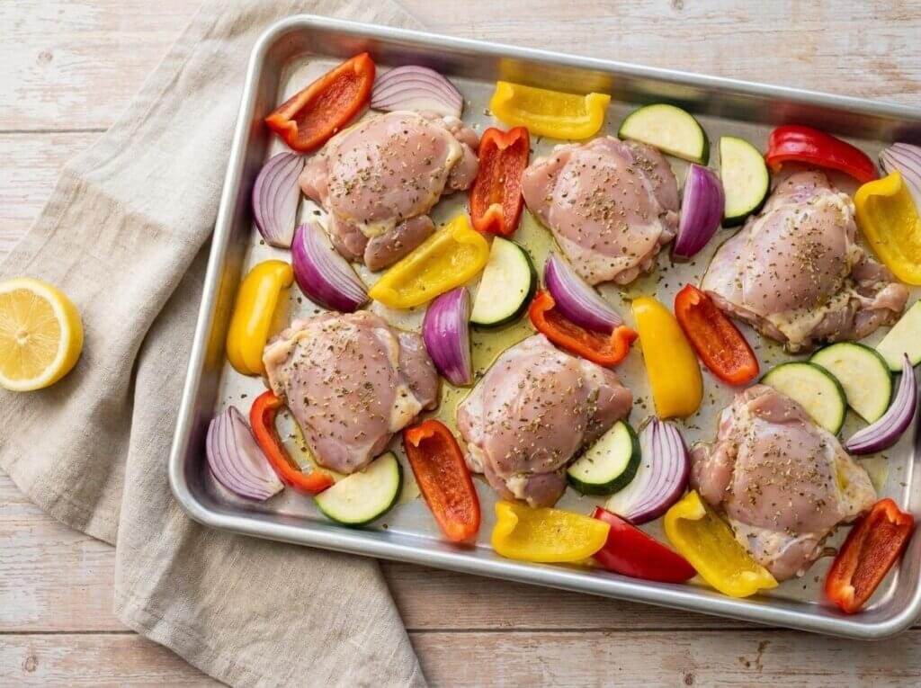 Marinated chicken thighs and vegetables on a sheet pan before roasting