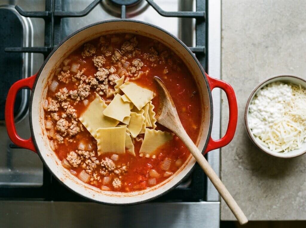 Broken lasagna noodles simmering in tomato broth with browned ground turkey in a Dutch oven