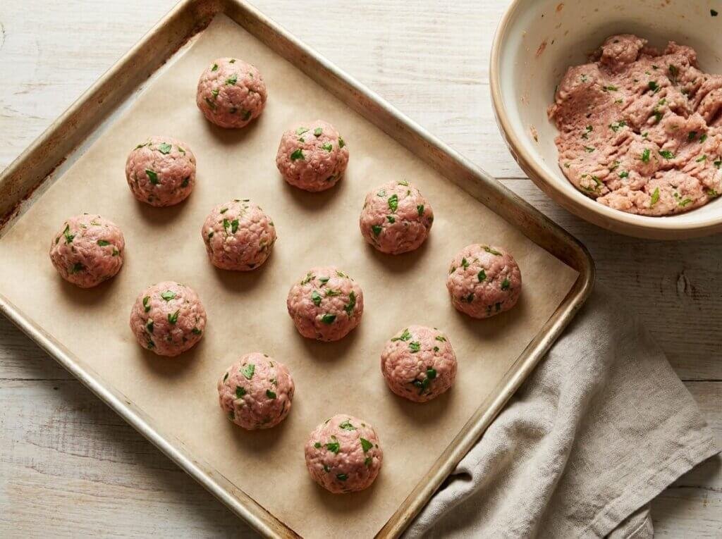 Shaped raw turkey meatballs on a parchment-lined baking sheet